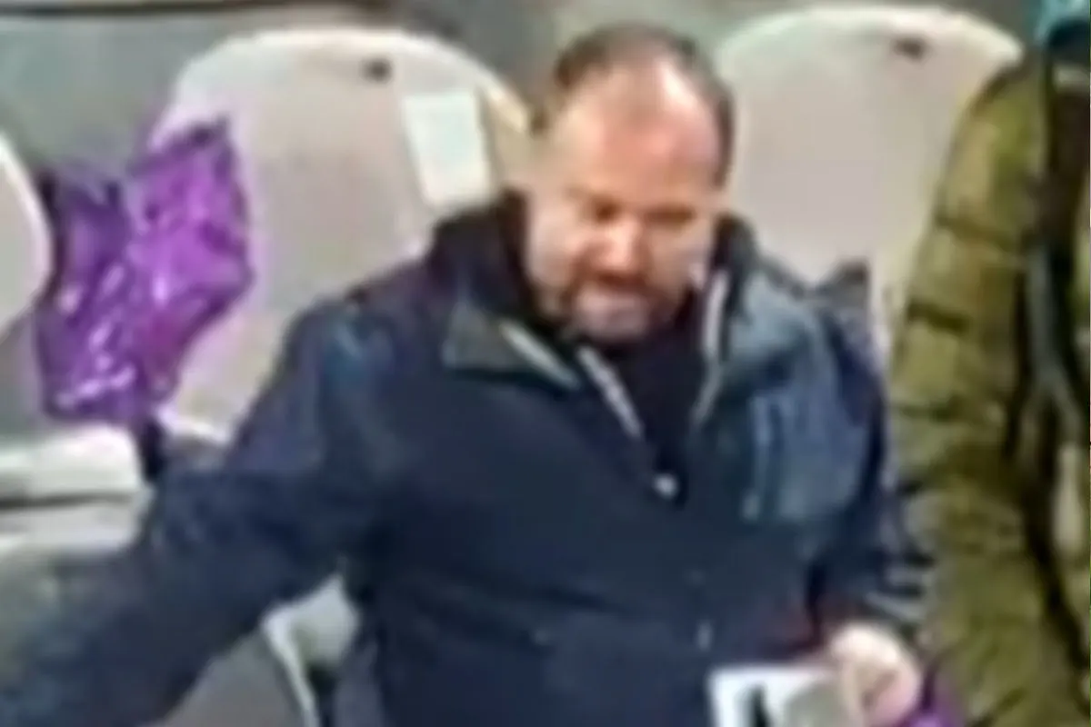 Eine Person trägt dunkle Kleidung und hält einen Gegenstand. Der Hintergrund ist verschwommen.