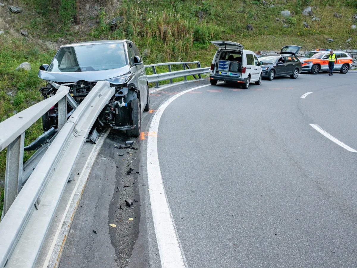 Ein silbernes Auto ist in einer Kurve gegen die Leitplanke geprallt, während hinten ein Polizeiauto und ein weiteres Fahrzeug stehen. Ein Polizist ist anwesend.