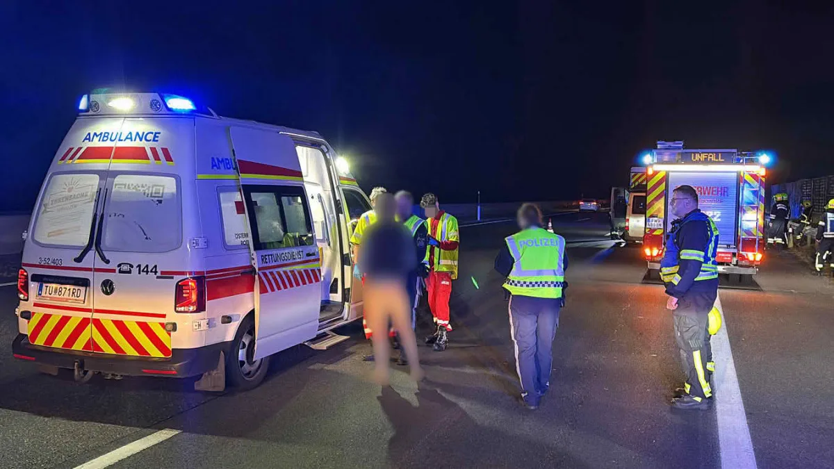 Bei Nacht stehen ein Rettungswagen und ein Feuerwehrfahrzeug auf einer Straße. Einsatzkräfte in Warnwesten kümmern sich um Betroffene.