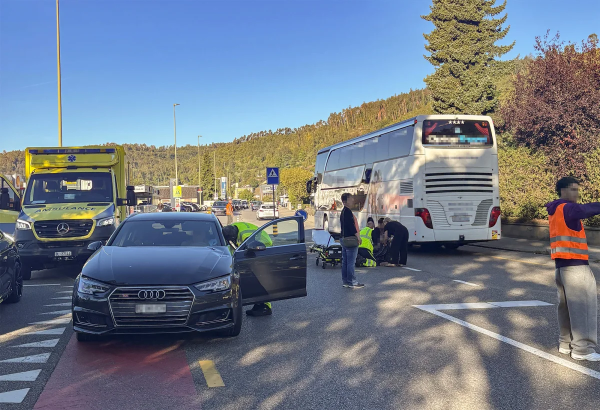 Sanitäter sind auf einer Straße beschäftigt, neben einem Bus und einem schwarzen Audi, während ein gelbes Rettungsfahrzeug bereitsteht. Eine Person mit orangefarbener Weste weist den Verkehr.
