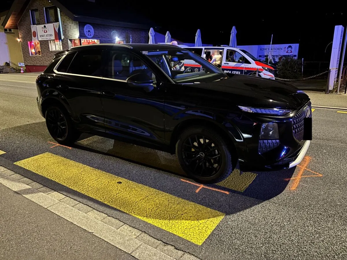 Ein schwarzer Audi steht quer auf der Straße, markiert mit Kreidezeichen. Im Hintergrund ist ein Polizeiwagen sichtbar.