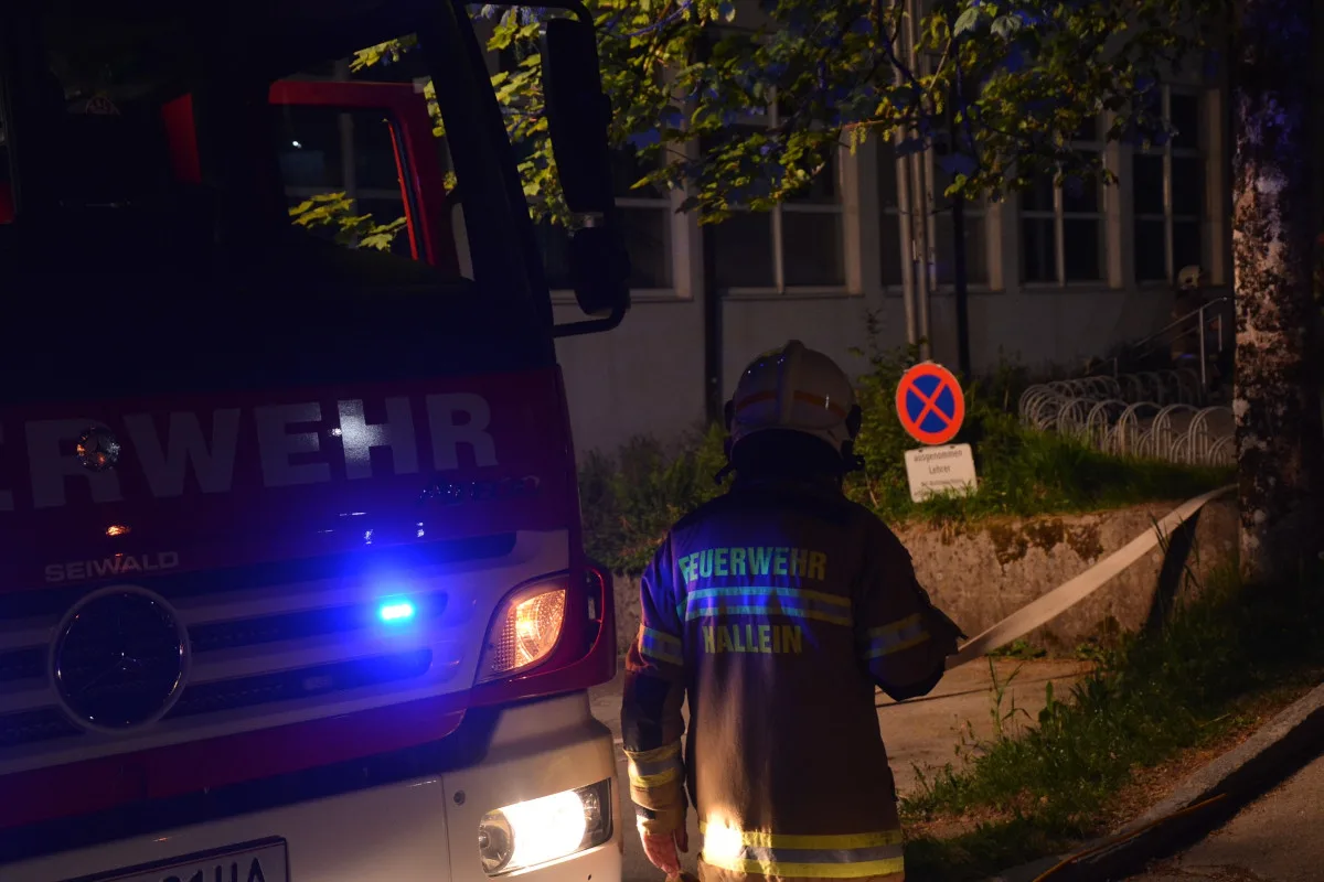 Ein Feuerwehrwagen mit eingeschaltetem Blaulicht steht in der Nacht. Eine Person in Feuerwehruniform steht daneben.