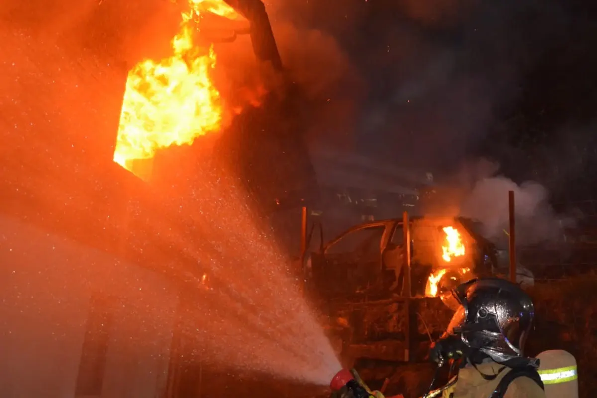 Ein Feuerwehrmann in Schutzkleidung löscht einen intensiven Brand an einem Gebäude mit einem Wasserschlauch bei Nacht.