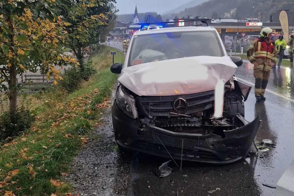 Ein Mercedes-Transporter mit erheblichen Frontschäden steht auf einer nassen Straße. Blaulicht ist aktiv, und Feuerwehrleute sind im Hintergrund sichtbar.