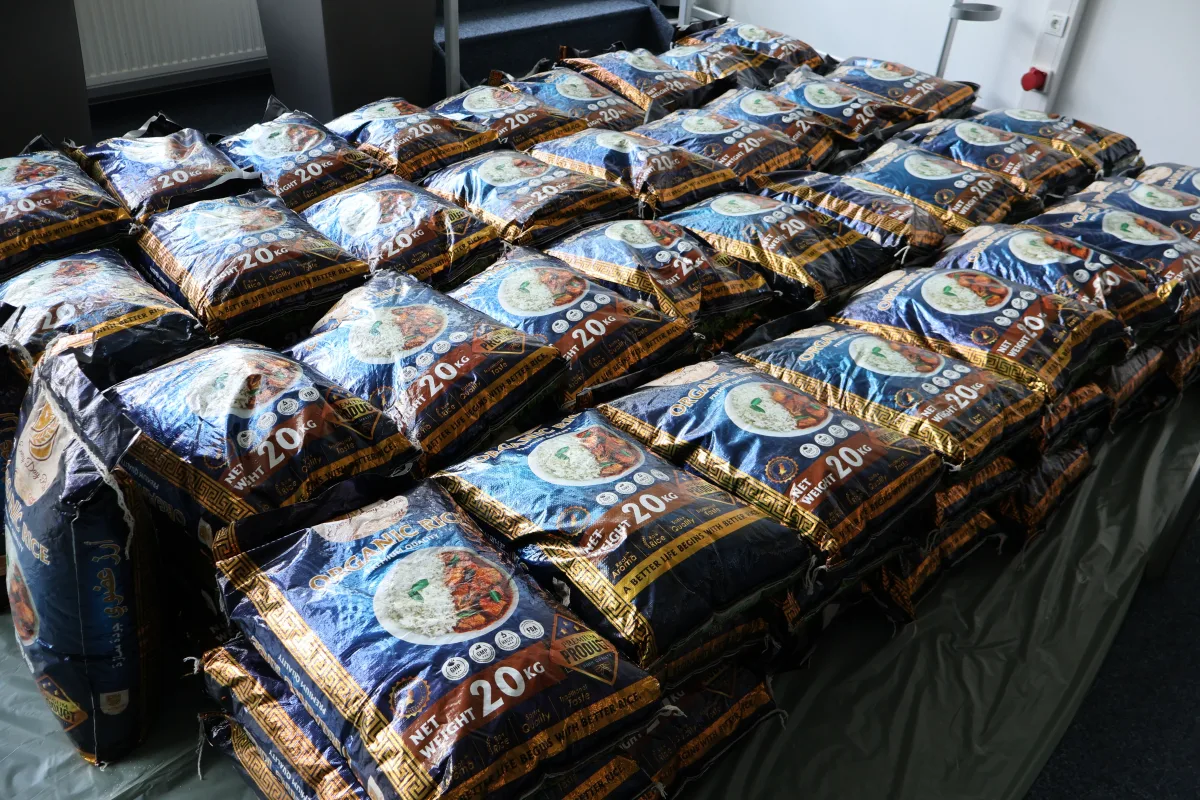 Auf einem Tisch sind zahlreiche große Reispackungen ordentlich gestapelt. Sie sind in blauen Verpackungen und jede wiegt 20 kg.