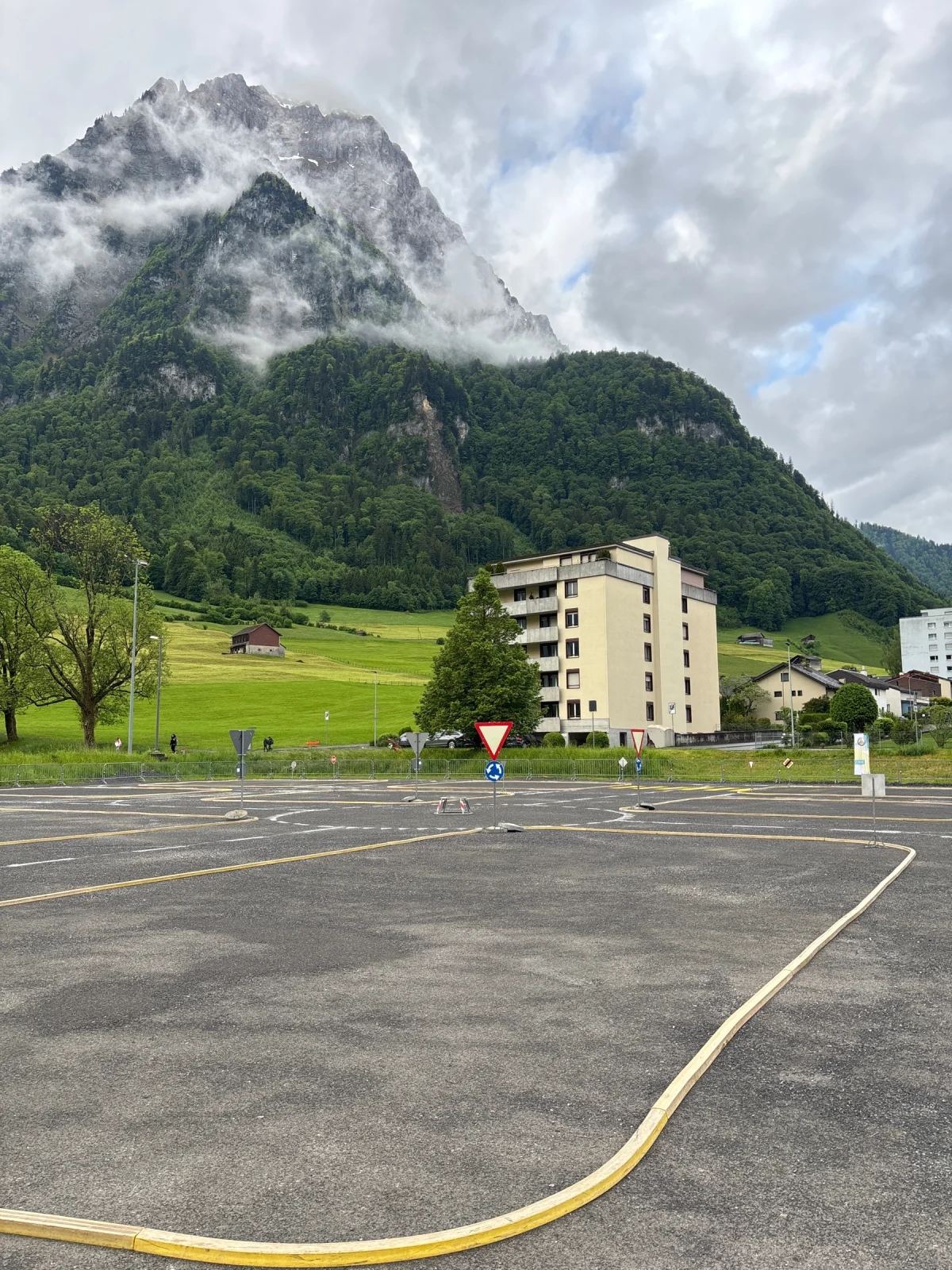 Ein hoher Berg erhebt sich in einer grünen Landschaft mit Wolken darüber. Im Vordergrund stehen Wohngebäude.