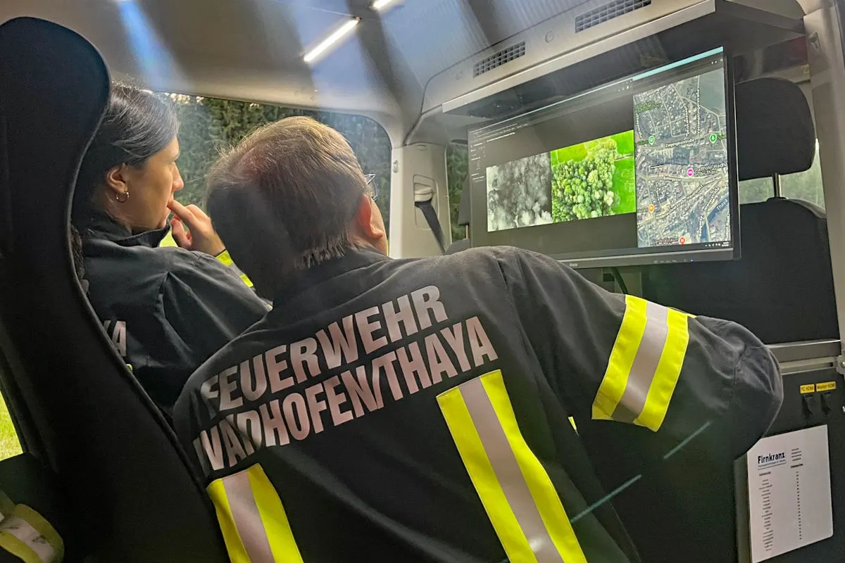Im Inneren eines Einsatzfahrzeugs betrachten zwei Feuerwehrleute Bildschirme mit Karten- und Drohnenaufnahmen.