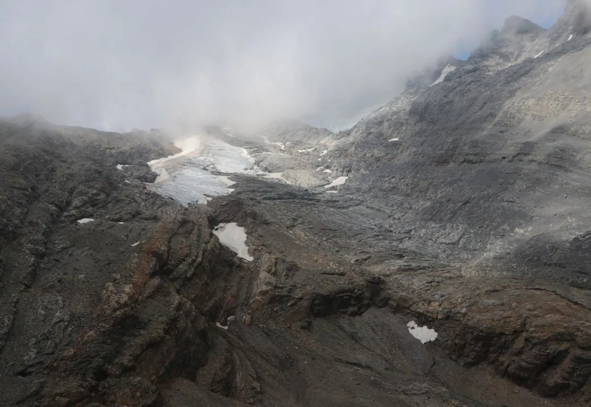 Eine alpine Landschaft zeigt einen Gletscher, der von Felsen umgeben ist, teilweise von Nebel verdeckt.