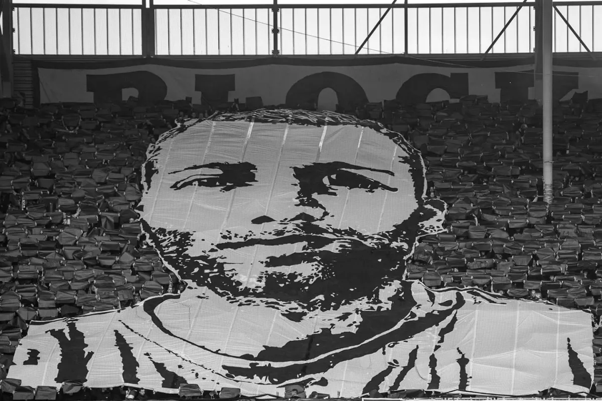 Ein großes Banner zeigt ein gezeichnetes Porträt eines Mannes, das über mehrere Sitzreihen in einem Stadion gespannt ist.