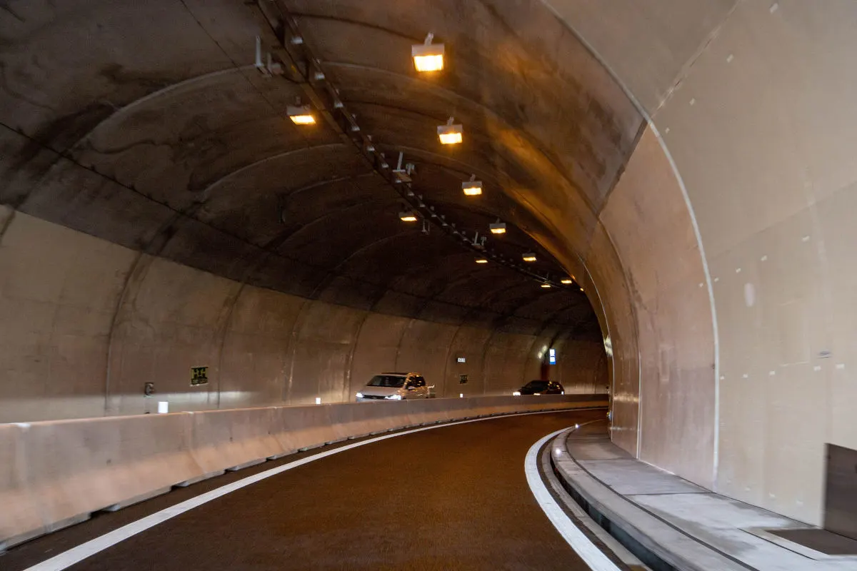 Ein beleuchteter Tunnel zeigt zwei Fahrzeuge, die durch den geschwungenen Tunnel fahren. Die Tunnelwände sind gut beleuchtet.
