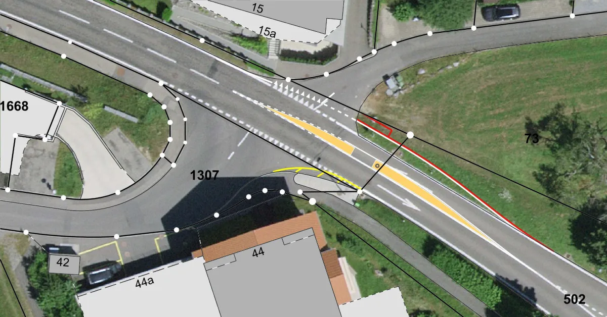 Eine Luftaufnahme zeigt eine Straßenkreuzung mit gelben Fahrbahnmarkierungen und umgebenden Gebäuden. Verschiedene Linien und Punkte markieren die Straßenplanung.