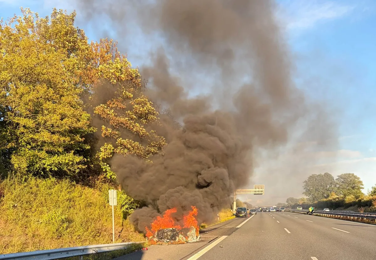Auf der Autobahn brennt ein Auto am Rande der Fahrspur, wobei dicker schwarzer Rauch aufsteigt und sich über die Straße ausbreitet.