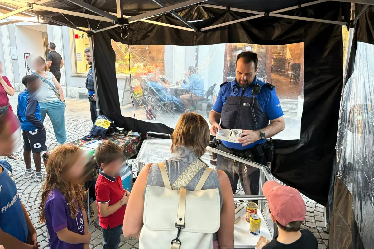 Ein Polizist steht an einem Stand und spricht mit einer Frau und mehreren Kindern. Im Hintergrund sind weitere Personen zu sehen.