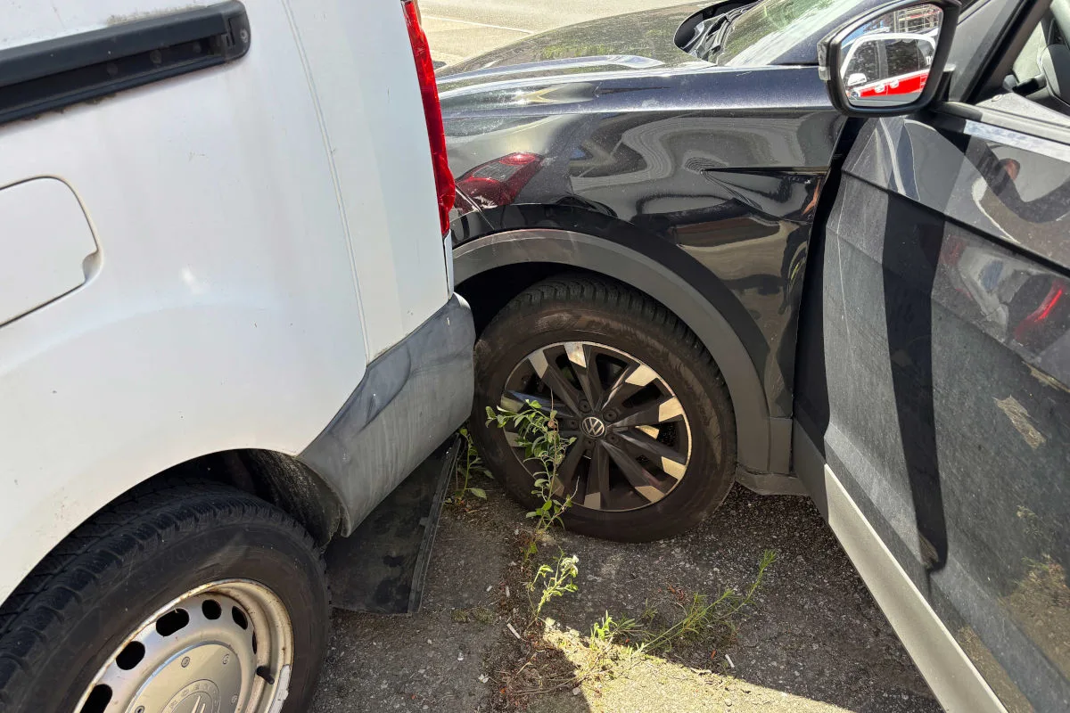 Ein weißer Van ist mit einem schwarzen VW auf einem Parkplatz zusammengestoßen, beide Fahrzeuge haben sichtbare Schäden.