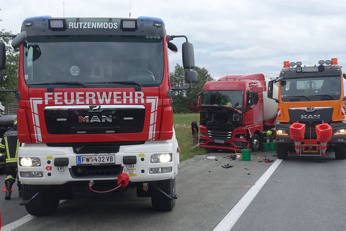 Ein rotes Feuerwehrfahrzeug mit der Aufschrift 'Rutzenmoos' steht auf der Straße. Daneben ist ein beschädigter roter Lkw zu sehen.