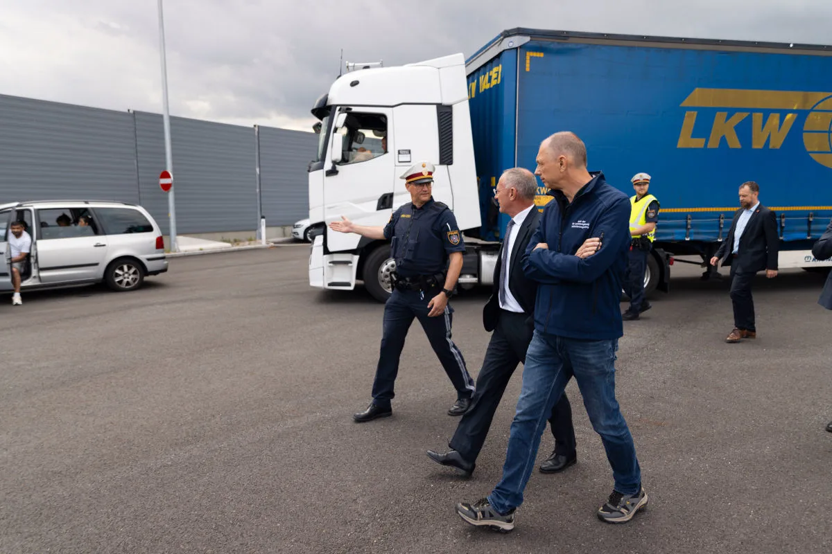 Ein Polizist unterhält sich mit zwei Männern in formeller Kleidung vor einem weißen LKW. Im Hintergrund ist ein weiteres Fahrzeug sichtbar.