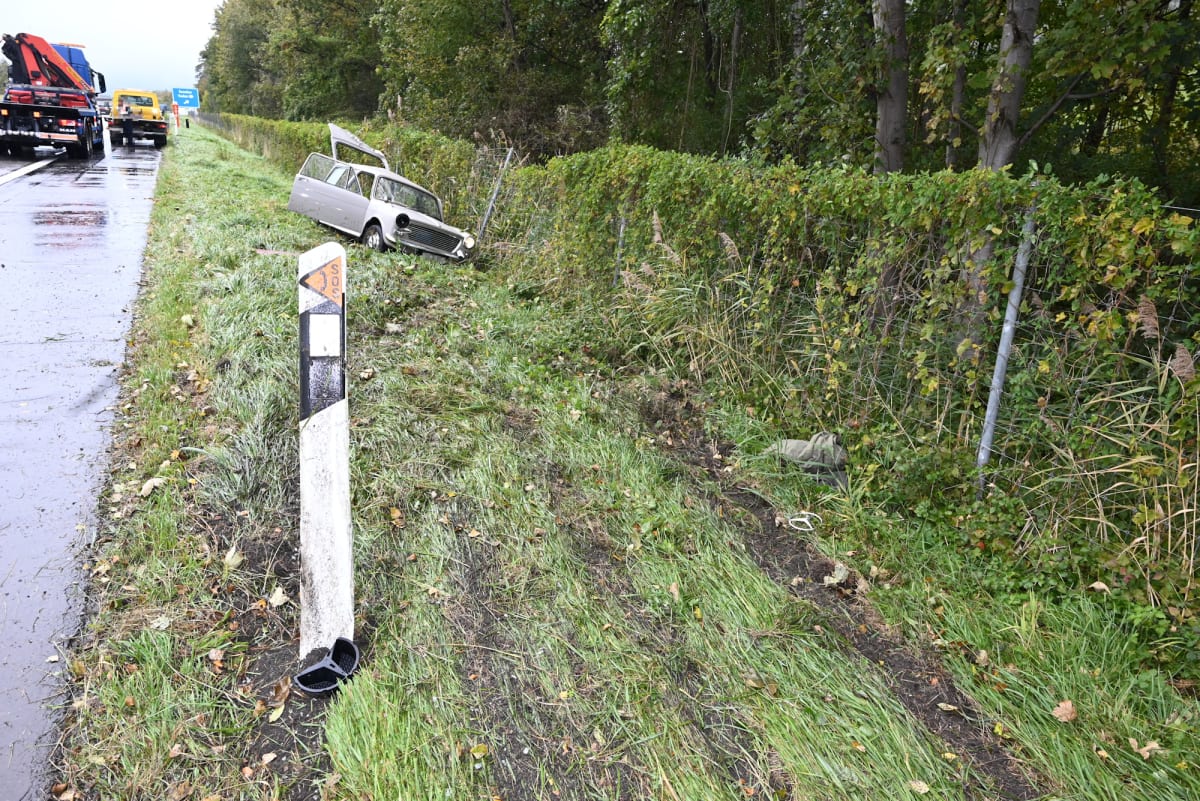 Ein silberfarbenes Auto liegt in einem Graben neben einer Autobahn. Der Leitpfosten ist verbogen, während ein Abschleppfahrzeug auf der Straße steht.