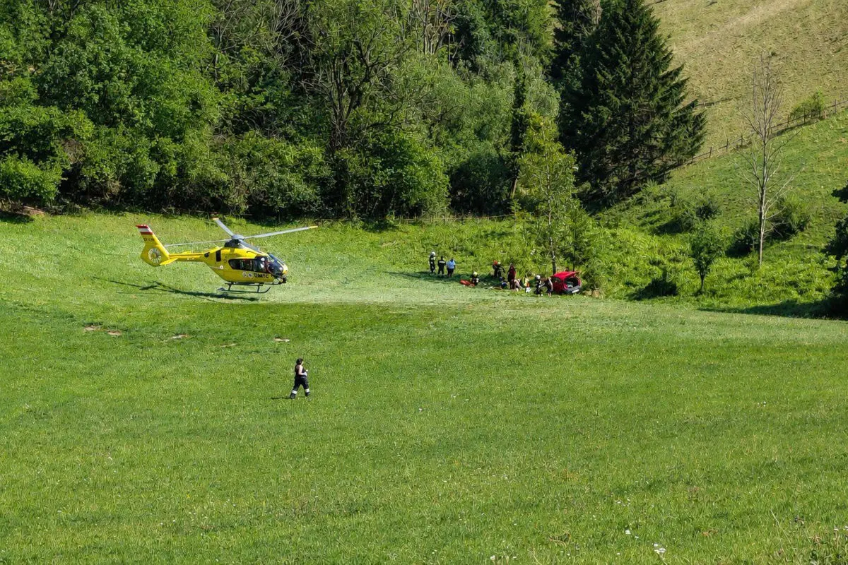Ein gelber Rettungshubschrauber steht auf einer Wiese, umgeben von Notfallhelfern, die auf einen Unfall reagieren.