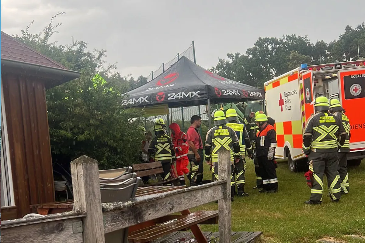 Eine Gruppe von Feuerwehrleuten und Rettungskräften steht neben einem Einsatzfahrzeug des Bayerischen Roten Kreuzes in einem grasbewachsenen Bereich.