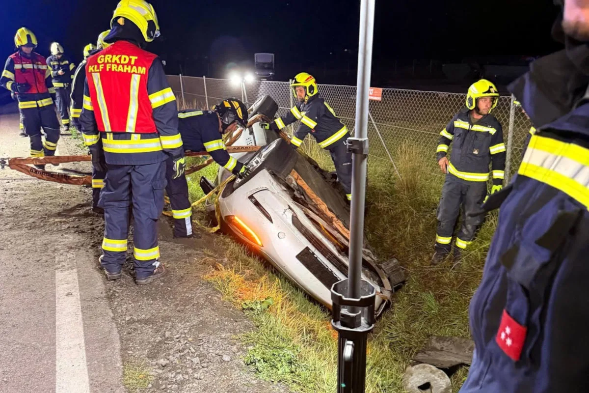Feuerwehrleute in Schutzkleidung arbeiten an einem auf der Seite liegenden Auto im Graben bei Nacht. Das Fahrzeug ist beschädigt.