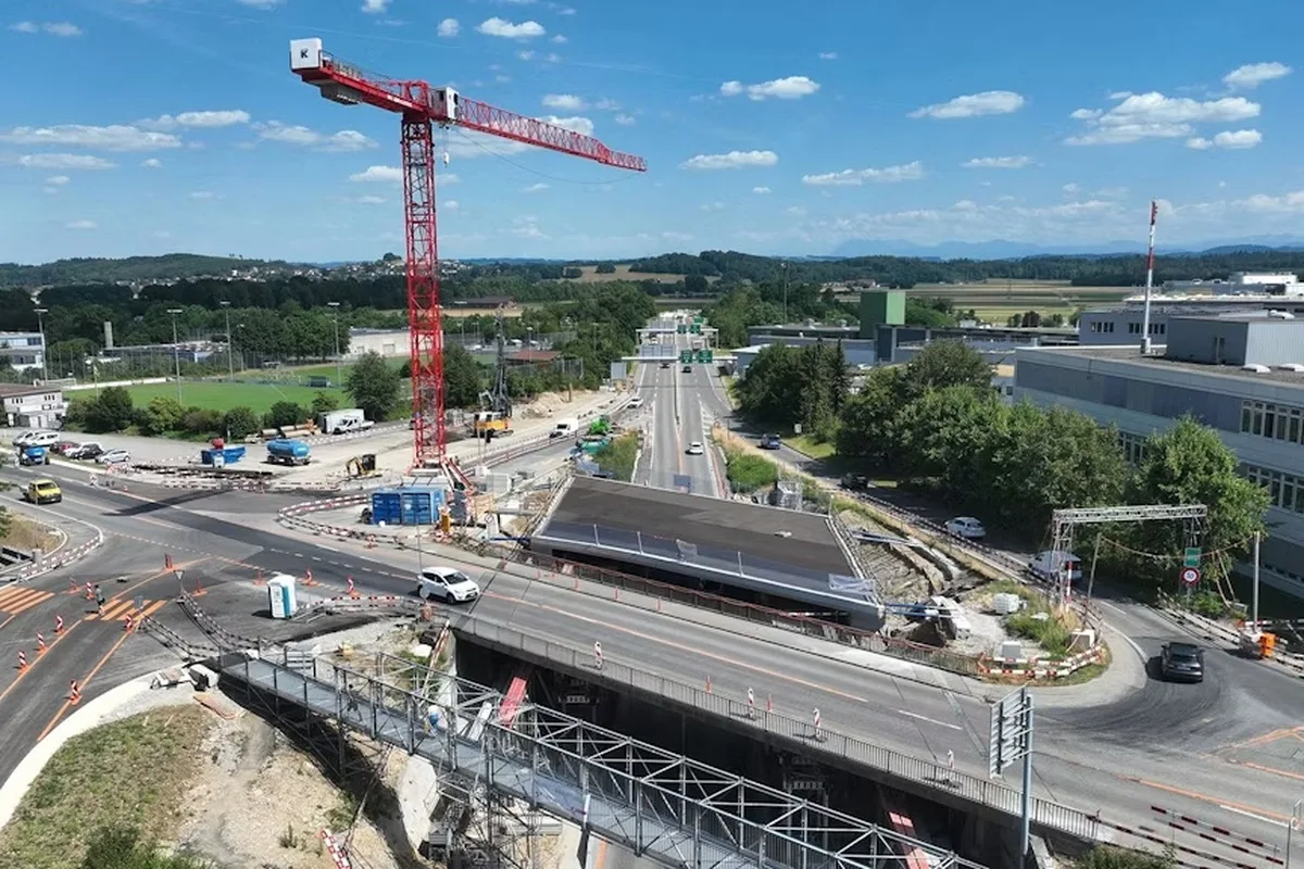 Ein großer, roter Kran steht über einer Straßenkreuzung, umgeben von einer Baustelle. Der Himmel ist klar und blau.