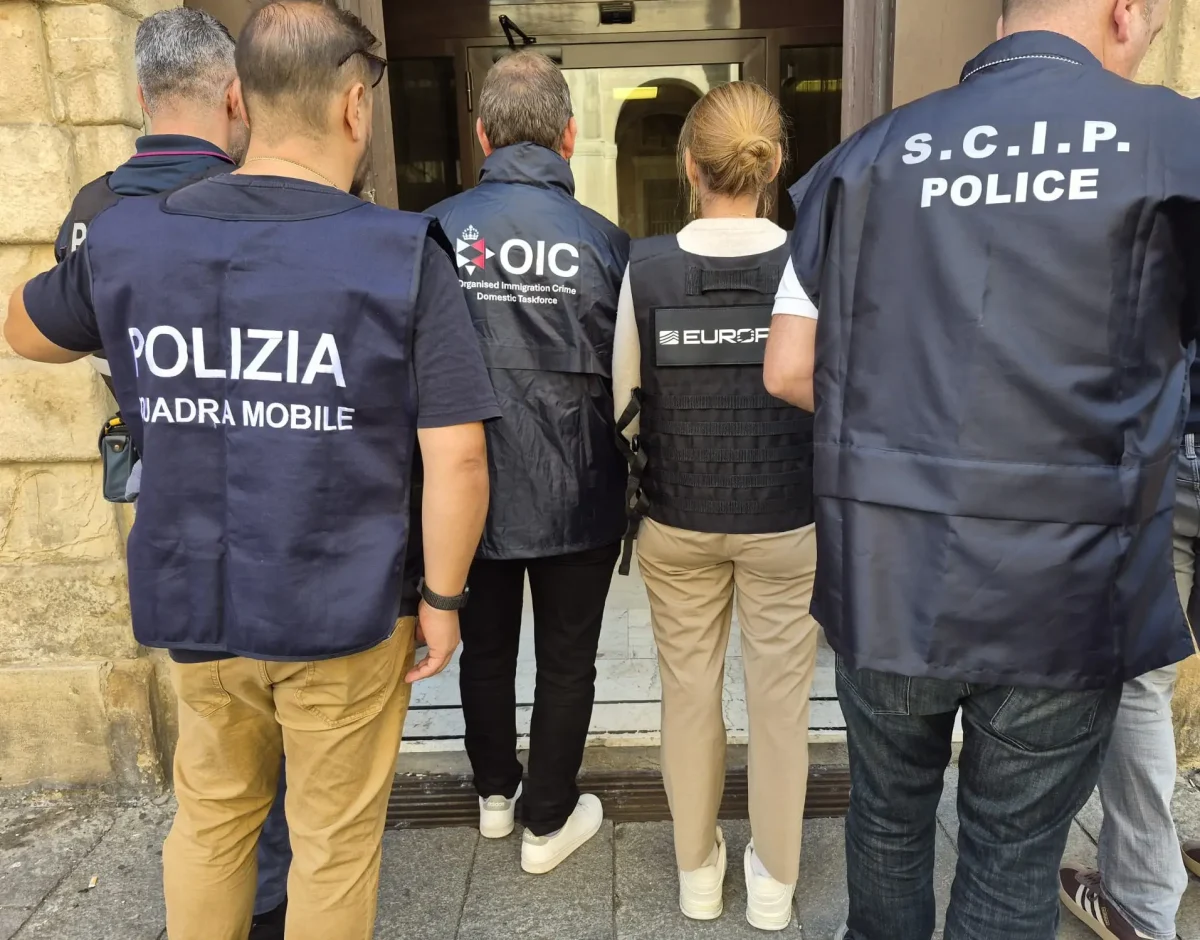 Eine Gruppe uniformierter Personen mit Westen mit Polizeiaufschriften steht vor dem Eingang eines Gebäudes.