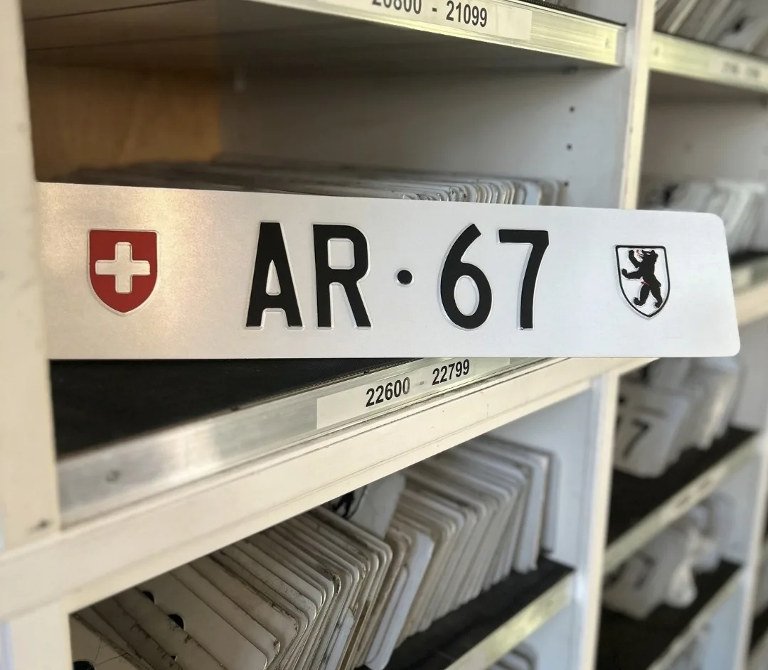 Ein altes Schweizer Nummernschild mit der Aufschrift 'AR 67' und Wappen von Appenzell wird in einem Regal aufbewahrt.