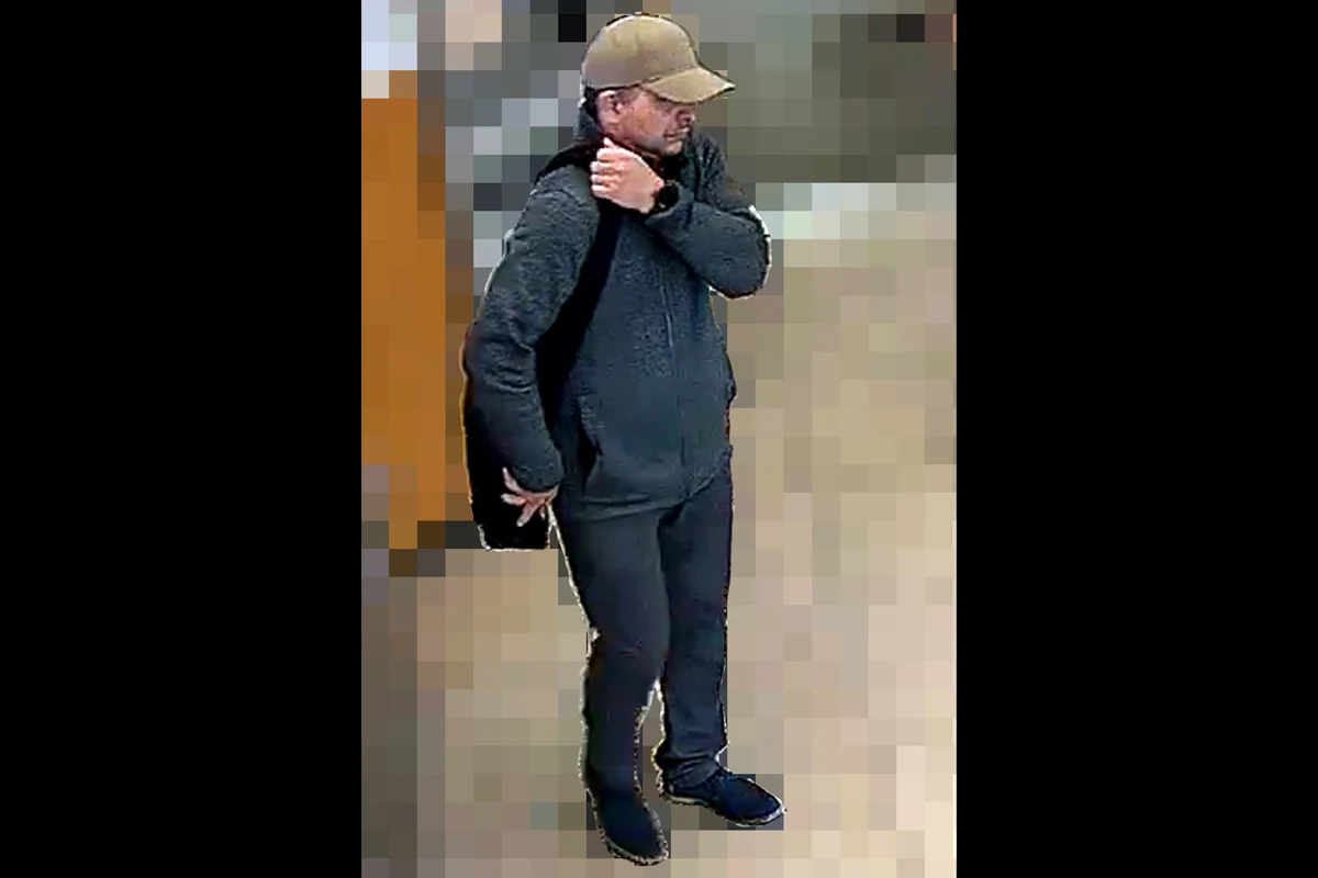 Ein Mann trägt eine beige Mütze und einen schwarzen Rucksack. Er befindet sich in einem Gebäude mit verschwommenem Hintergrund.