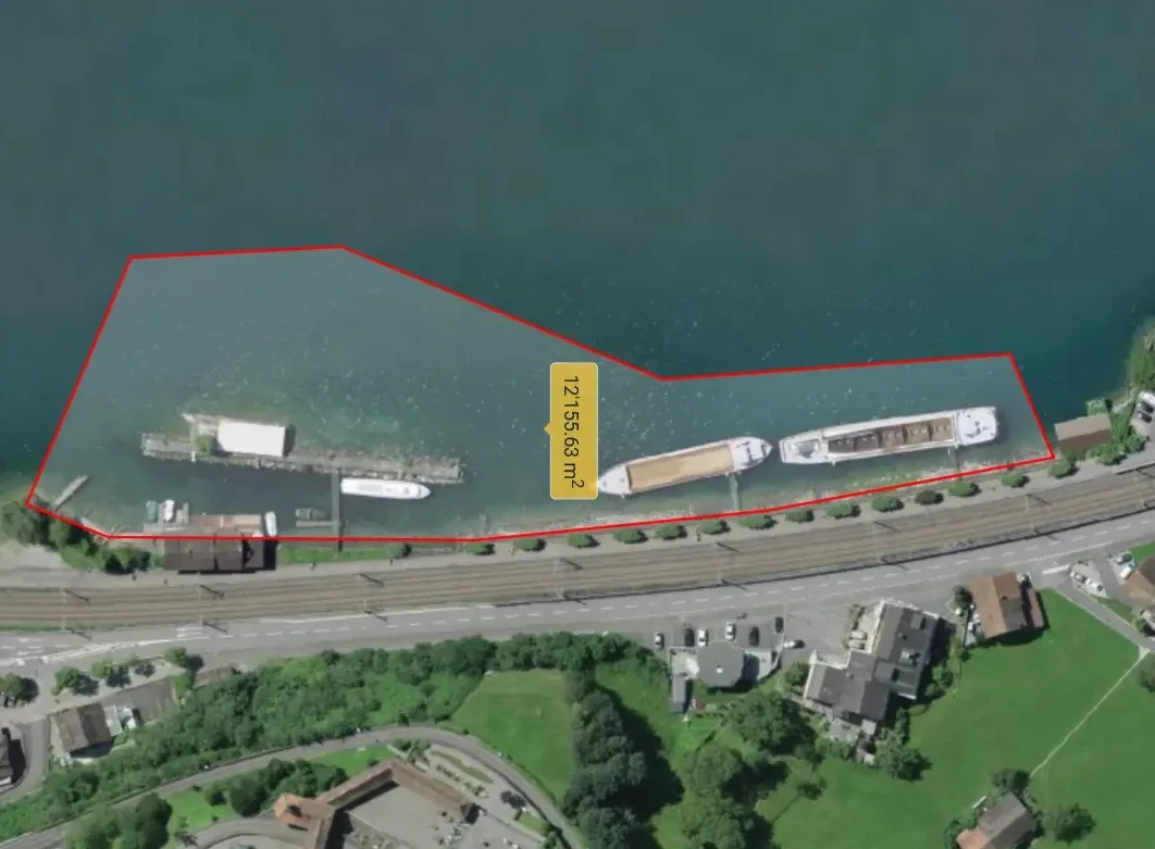 Das Luftbild zeigt eine eingezeichnete, polygonale Fläche im Wasser, an der mehrere Schiffe festgemacht sind. Unten im Bild ist eine Straße zu sehen.