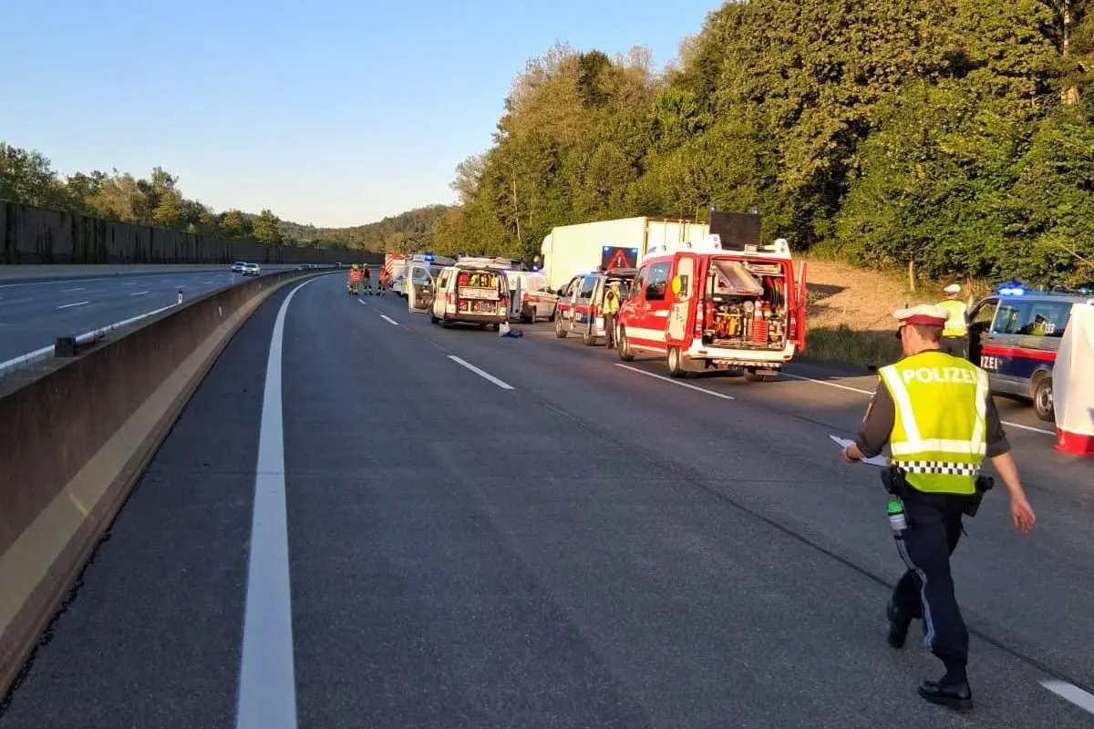 Ein Polizist in gelber Weste steht auf einer Autobahn neben mehreren Einsatzfahrzeugen. Die Straße ist gesperrt.