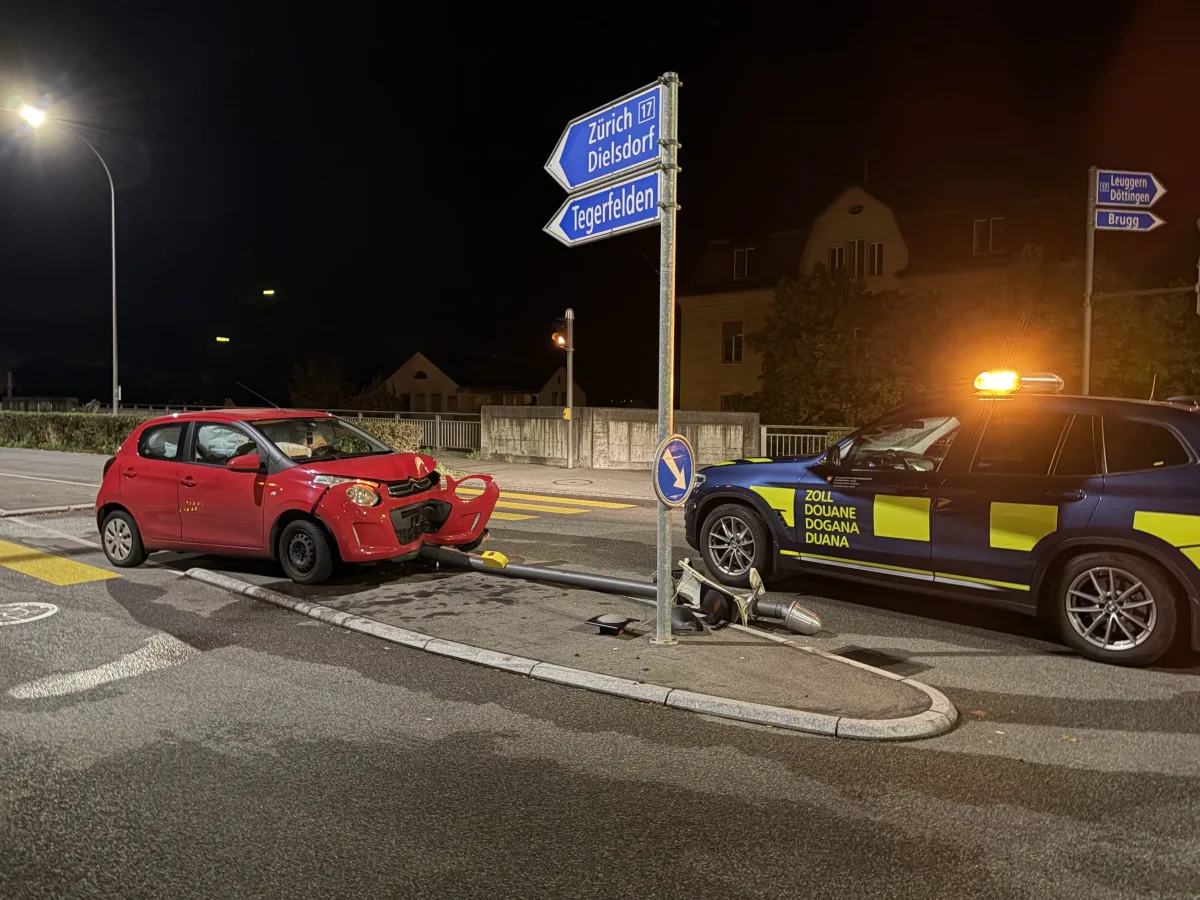 Ein rotes Auto ist bei Nacht gegen ein Verkehrszeichen geprallt. Ein Zollfahrzeug ist daneben geparkt.