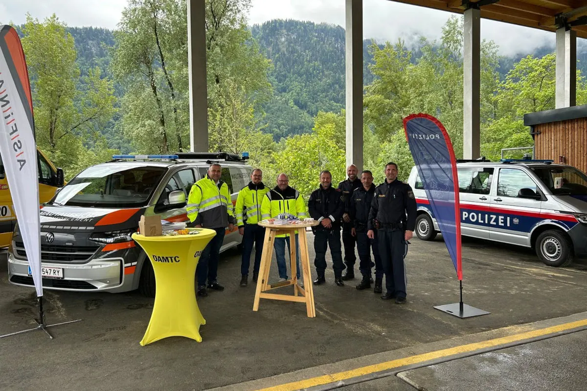 Mehrere Polizisten und Personen in Warnwesten stehen unter einer Überdachung neben österreichischen Polizeiautos und einem gelben Tisch.