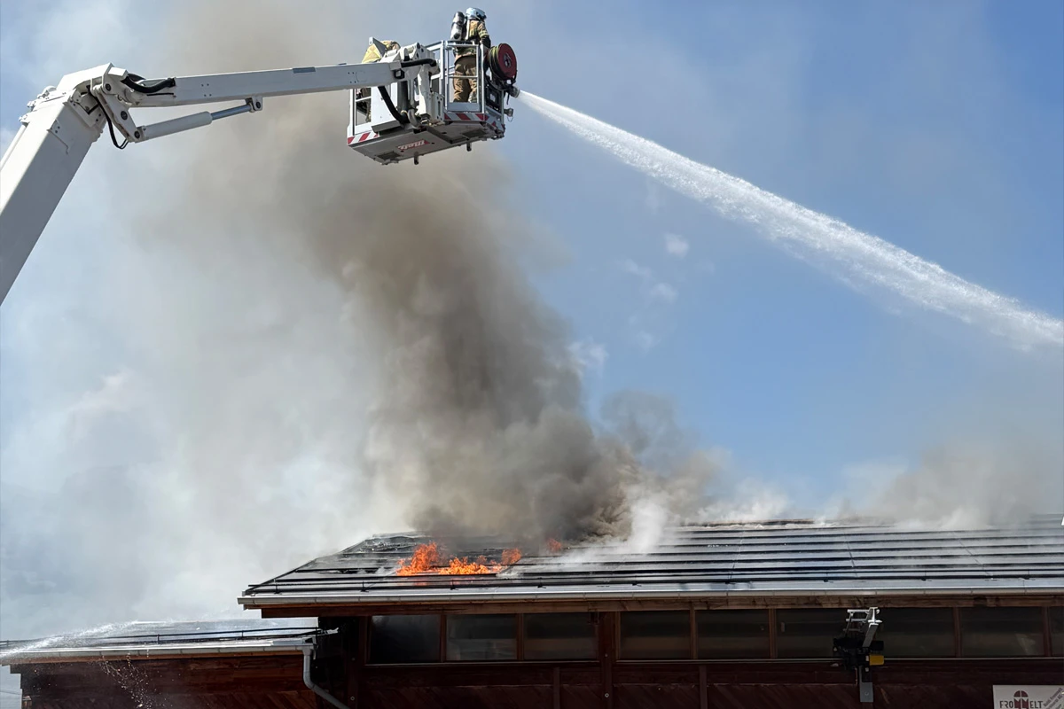 Ein Feuerwehrmann in einem Hubsteiger bekämpft einen Brand auf dem Dach eines Gebäudes mit einem Wasserstrahl.