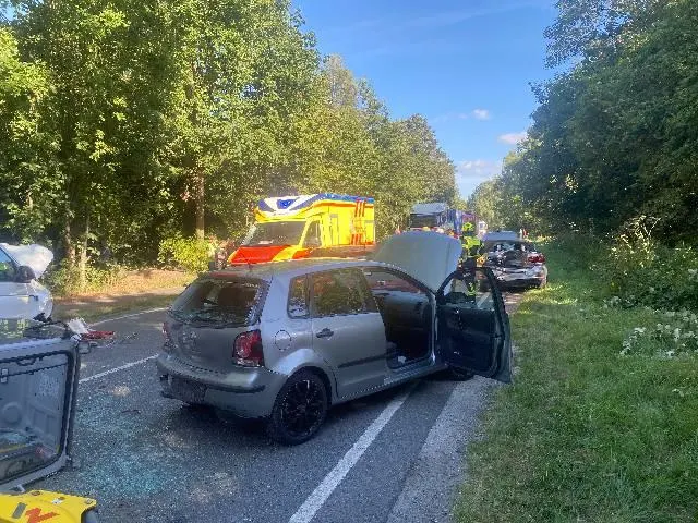Auf einer Landstraße steht ein graues Fahrzeug mit geöffneten Türen. Im Hintergrund ist ein Rettungswagen zu sehen.