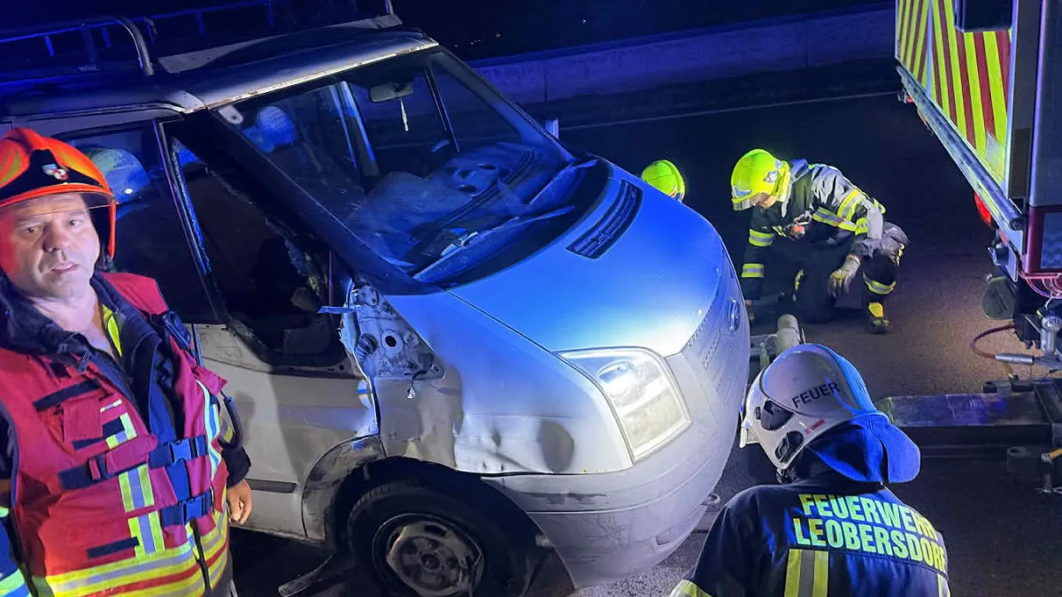Drei Feuerwehrleute untersuchen bei Dunkelheit einen beschädigten weißen Transporter. Einer steht links, die anderen knien.