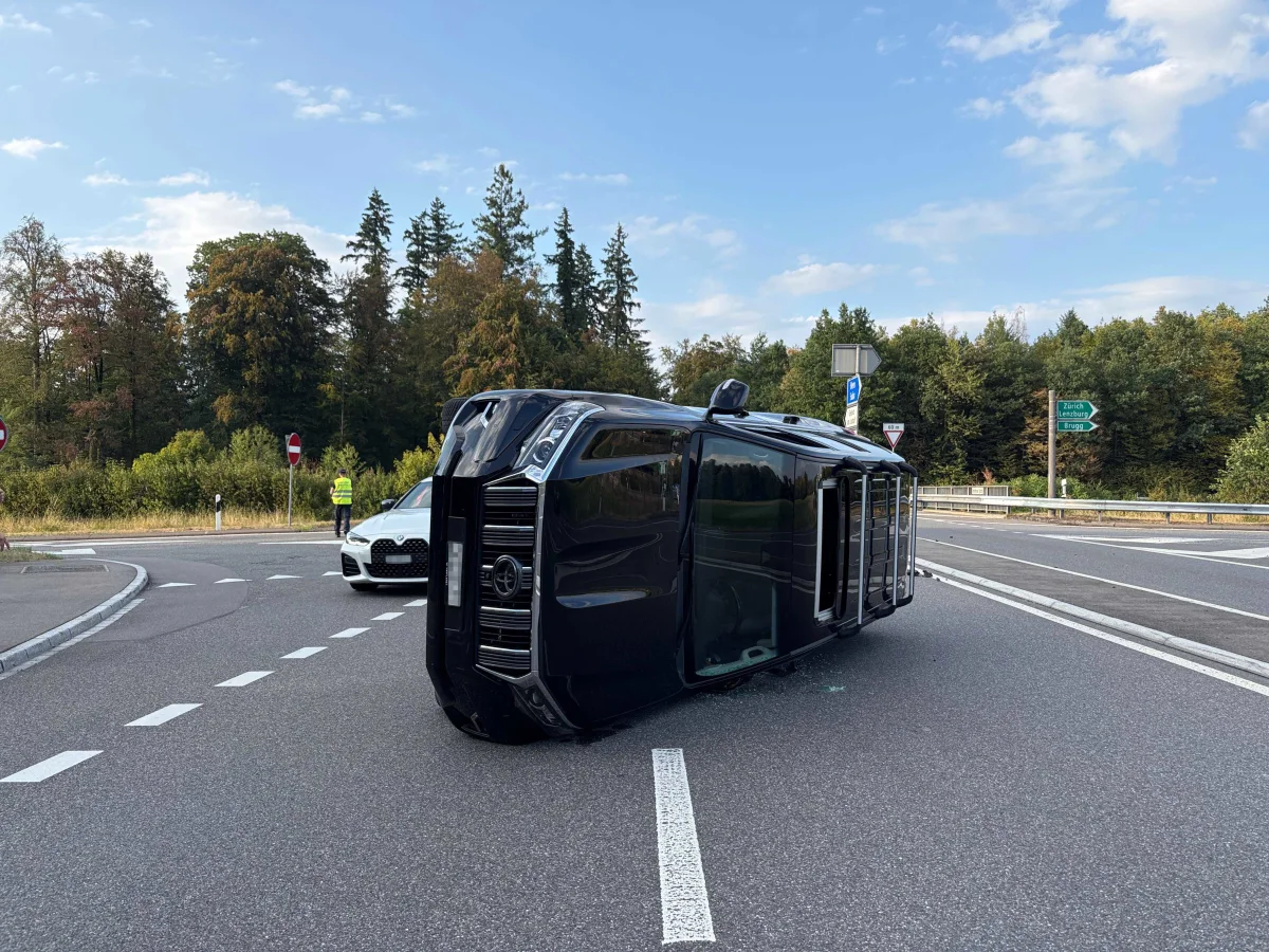 Ein schwarzer SUV liegt seitlich auf einer Kreuzung, im Hintergrund steht ein weißes Auto und ein Mann in gelber Weste.