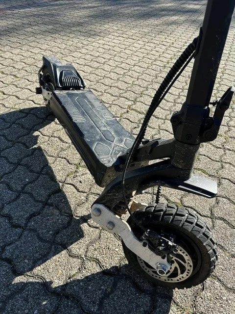 Ein beschädigter E-Scooter liegt auf einem gepflasterten Weg. Der Vorderteil ist abgebildet.