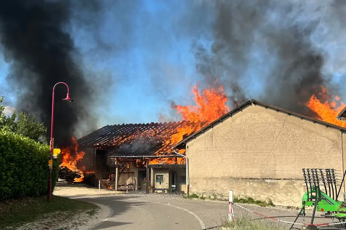 Ein landwirtschaftliches Gebäude brennt heftig, Flammen schlagen aus dem Dach und dichter Rauch steigt in den Himmel.