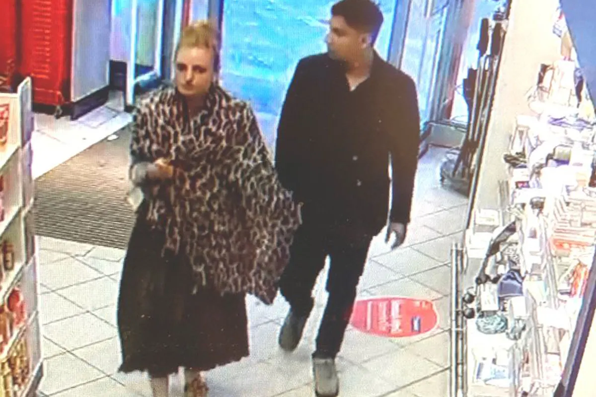 Ein Mann und eine Frau werden von einer Überwachungskamera erfasst, während sie einen Laden betreten. Beide Personen sind lässig gekleidet.