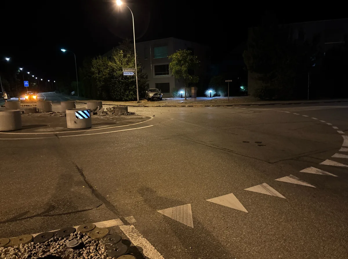 Bei Nacht ist ein Auto auf einem Bordstein verunfallt. Straßenlampen beleuchten die Szene schwach, Teile des Bordsteins sind beschädigt.
