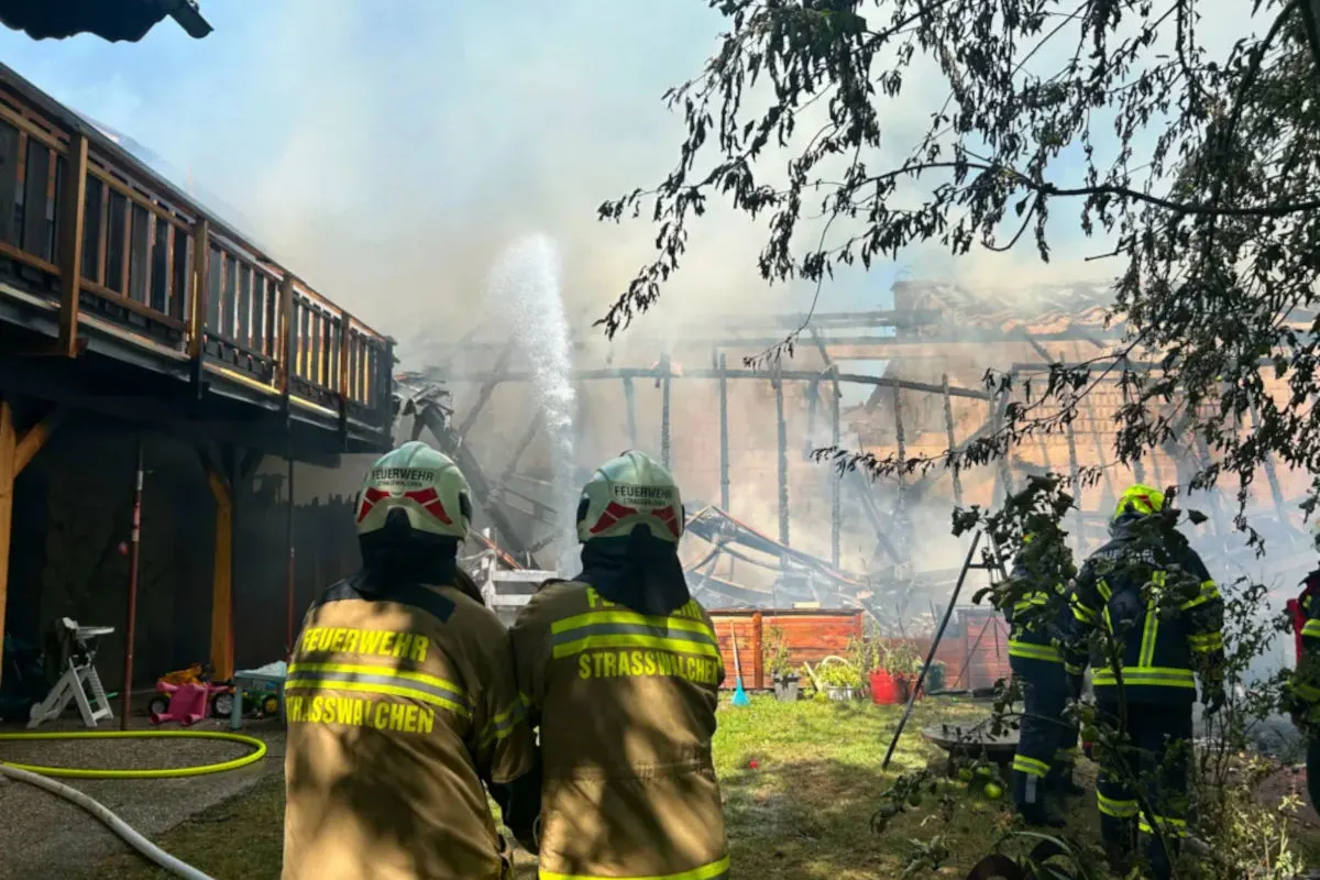 Zwei Feuerwehrleute in Schutzkleidung bekämpfen ein Feuer an einem einstürzenden Gebäude. Wasser wird auf die Flammen gespritzt.
