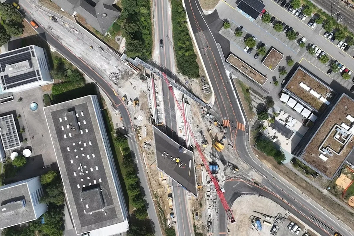 Eine Luftaufnahme zeigt umfangreiche Bauarbeiten an einer Straßenkreuzung, umgeben von Geschäftsgebäuden und Parkplätzen.