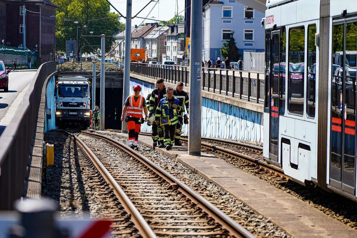 Drei Rettungskräfte in Schutzkleidung gehen auf Bahngleisen. Ein MAN-Lkw steht zwischen Gleisen und einer vorbeifahrenden Straßenbahn.