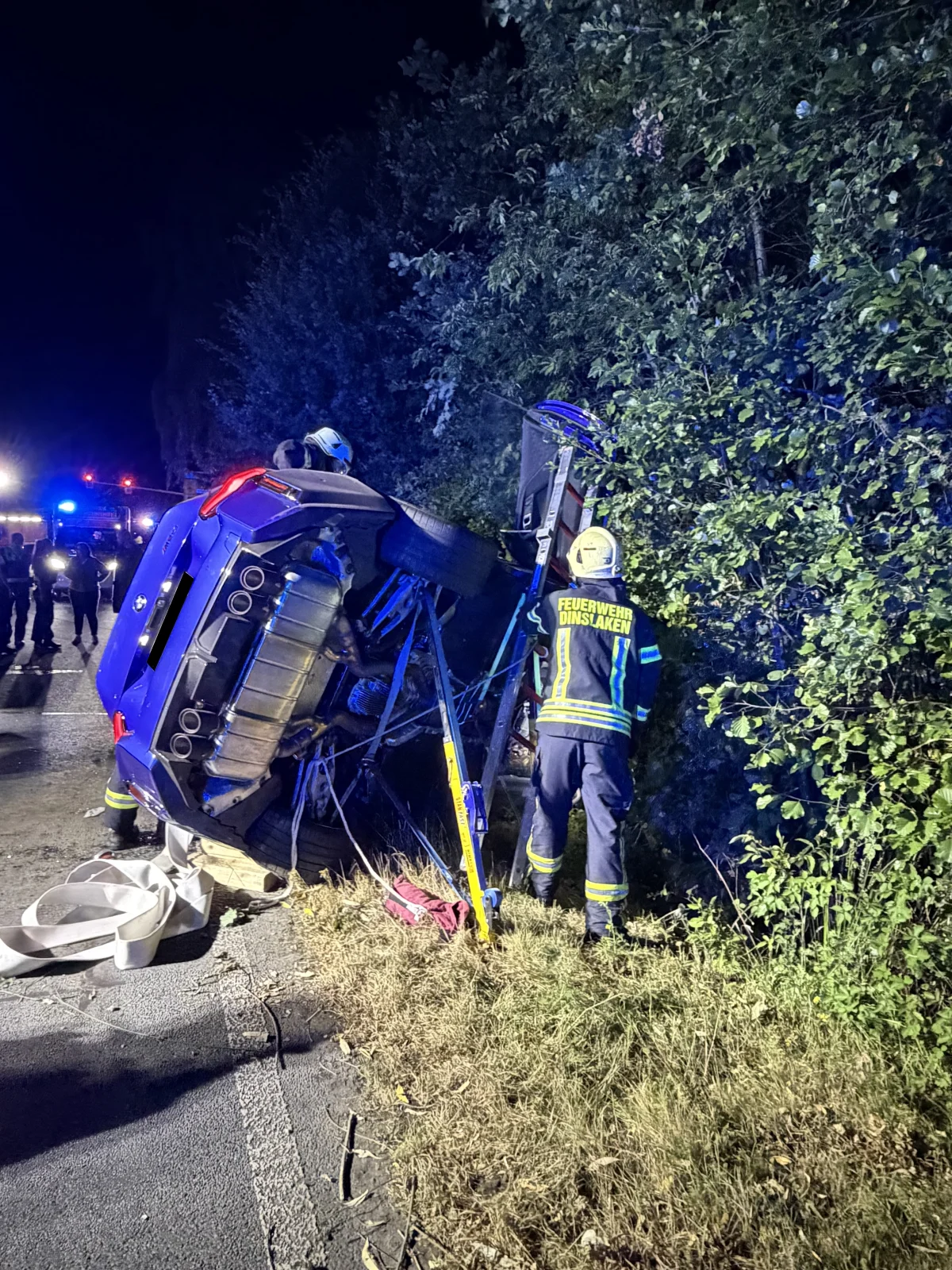Ein Feuerwehrmann steht neben einem auf die Seite gekippten Auto am Straßenrand. Es ist Nacht, und der Unfallwagen liegt im Graben.