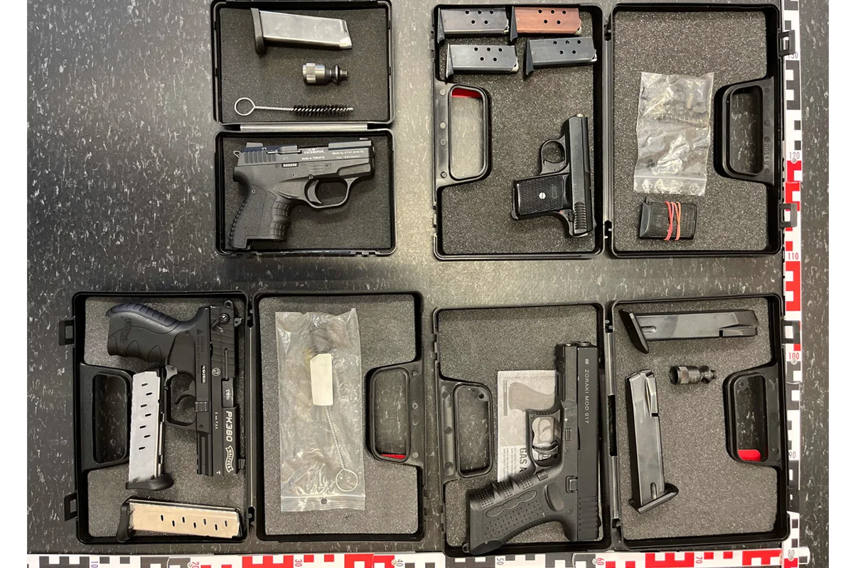 Auf einem Tisch liegen mehrere geöffnete Koffer, die Handfeuerwaffen, Magazine und Reinigungsutensilien enthalten. Die Szene zeigt polizeiliche Beweismaterialien, die geordnet präsentiert werden.