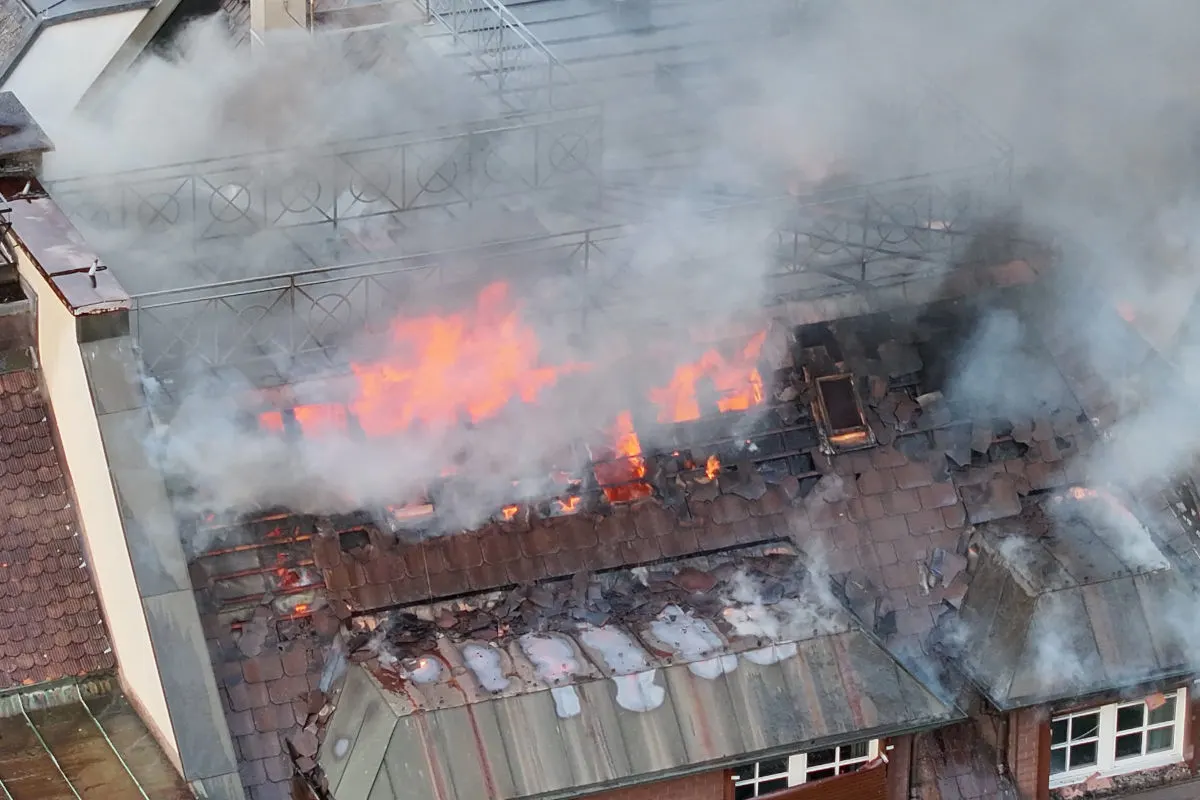Das Bild zeigt ein stark brennendes Dach mit Flammen und dichter Rauchentwicklung. Die Zerstörung am Dach ist deutlich erkennbar.