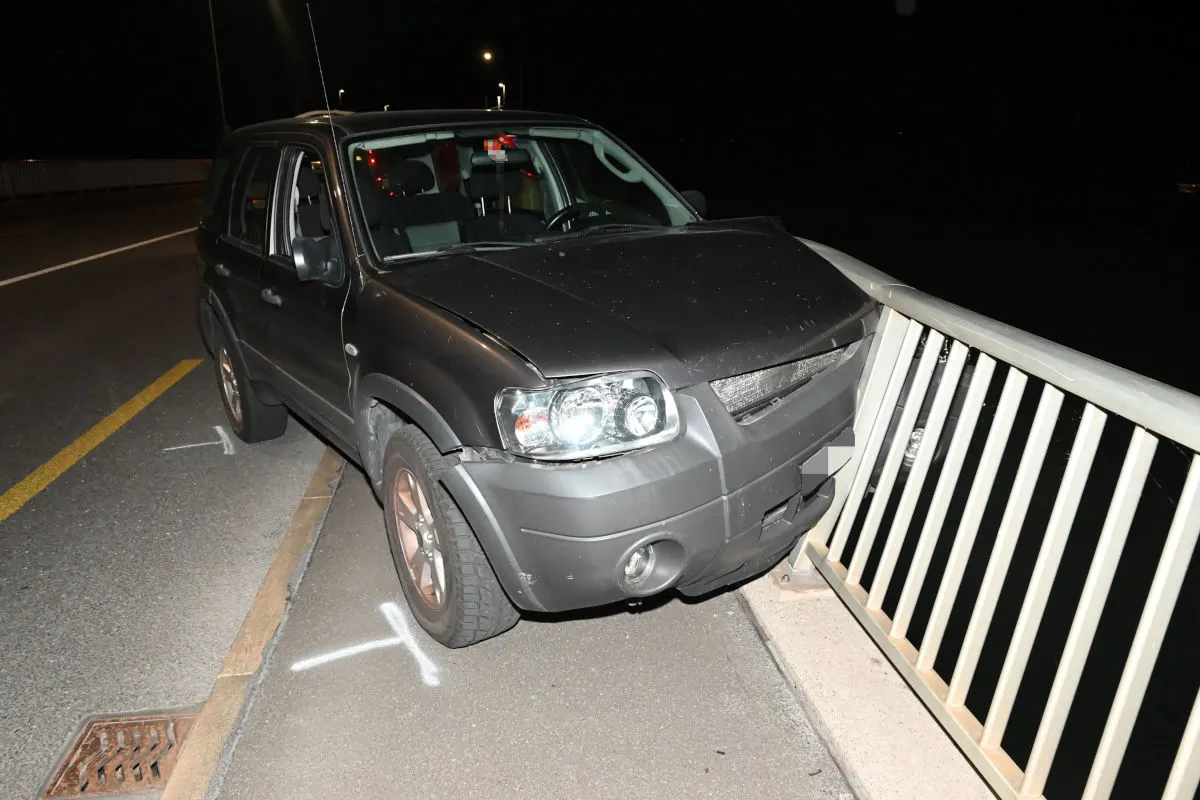 Ein dunkelgrauer SUV ist frontal mit einem Brückengeländer kollidiert. Die vordere Stoßstange ist eingedrückt, es sind keine Personen sichtbar.