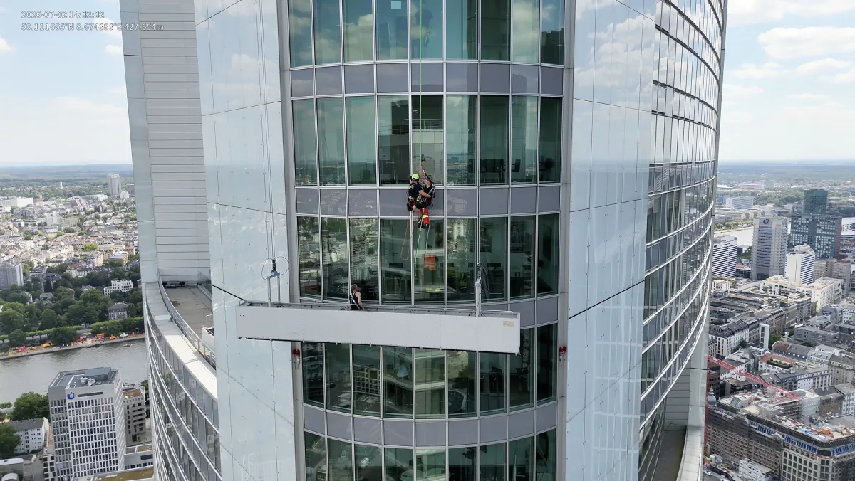 Höhenretter der Feuerwehr seilen sich von der Fassade eines Frankfurter Wolkenkratzers ab, um eine Person zu bergen. Im Hintergrund erstreckt sich die Stadtlandschaft.