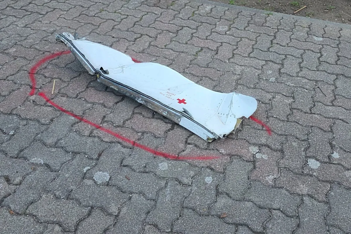 Auf einem Gehweg liegt ein Teil eines Flugzeuges mit sichtbaren Schäden, umgeben von einer roten Kreismarkierung.