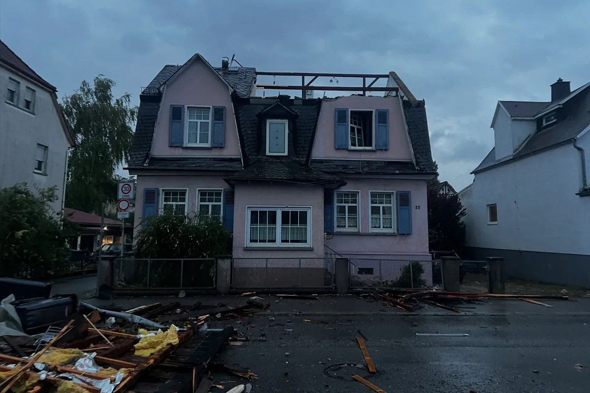 Ein zweigeschossiges Haus mit rosa Fassade hat ein zerstörtes Dach, vermutlich durch Sturm. Auf der Straße davor liegen Trümmerteile.